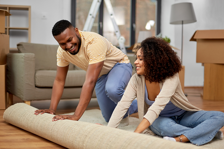 Couple rolling out carpet together in living room.